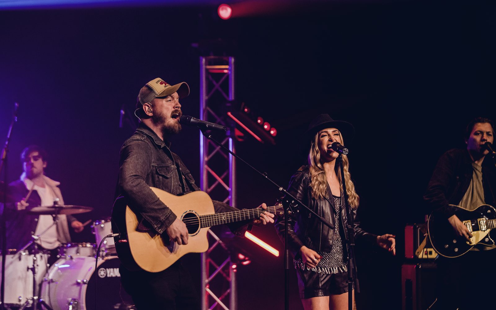 Two Nashville At Heart vocalists singing together under red and amber light