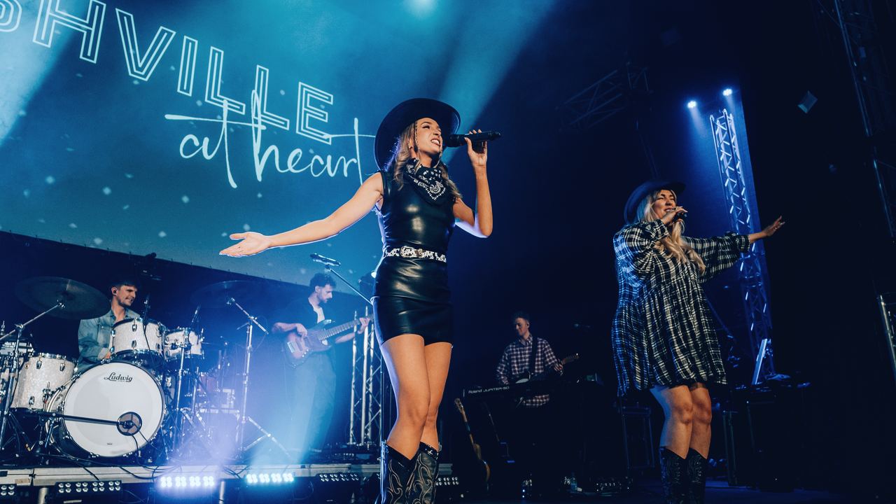 Two Nashville At Heart vocalists on stage in front of the show's illuminated logo
